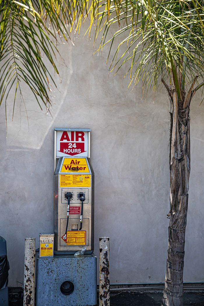 An air and water machine located at a sunny gas station with a palm tree beside it.